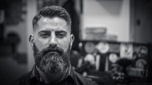 Minoxidil barba; imagen en blanco y negro y con un fondo desenfocado, mostrando el primer plano de un hombre serio con barba abundante al emplear el Minoxidil.