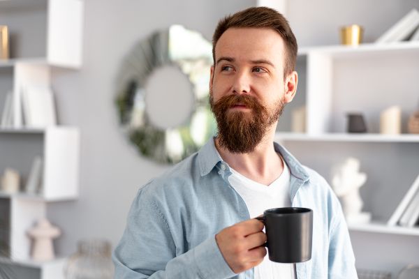 Minoxidil barba; presentación de una imagen con un plano medio corto de un hombre con barba sosteniendo una taza de café en una habitación.